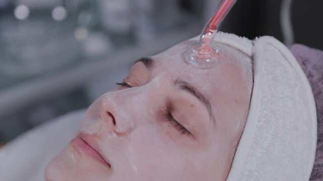 Receiving electric darsonval facial massage procedure.