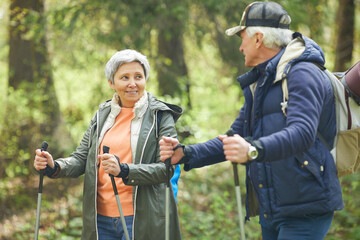 Waist up portrait of active senior couple enjoying Nordic walking with poles during hike in forest