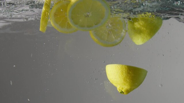 cut lemons droped into the transparent aquarium with water on grey background Slow motion from 120 fps