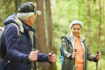 Fototapeta premium Waist up portrait of active senior woman enjoying Nordic walking during hike in forest with husband, copy space