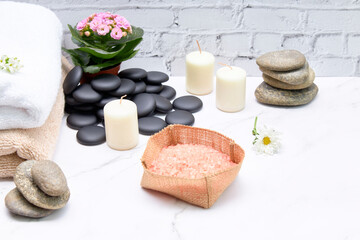 Spa bath salts next to some towels and candles on a marble table