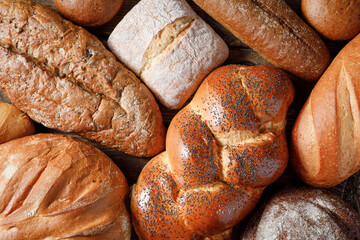 Variety of loaves of bread and buns on wooden table background.