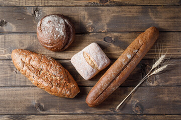 Variety of loaves of bread and buns on wooden table background.