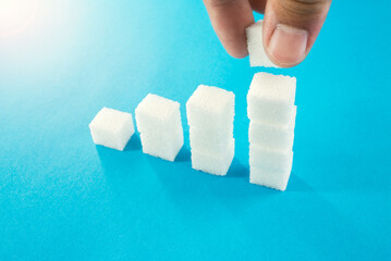 degree of sugar cubes on a blue background man's hand makes a cube. diabetes mellitus.