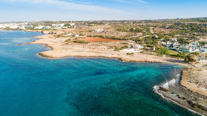 Fototapeta premium Aerial bird's eye view of Ammos tou Kambouri beach, Ayia Napa, Cavo Greco, Famagusta, Cyprus. Tourist attraction bay, rocky beach with golden sand, sunbeds, sea restaurant in Agia Napa from above.