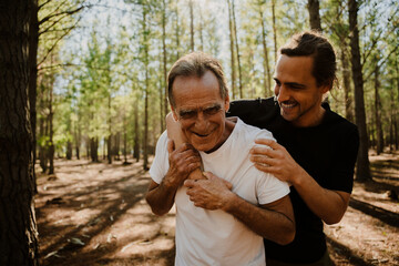 Father and adult son hugging and laughing together in the woods after a run