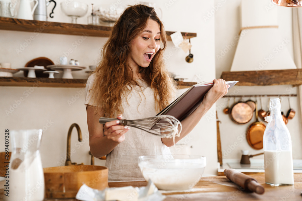 Wall mural Attractive young cheerful girl baking at the kitchen