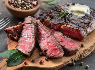 Medium rare Ribeye steak with herbs and a piece of butter on the wooden tray.