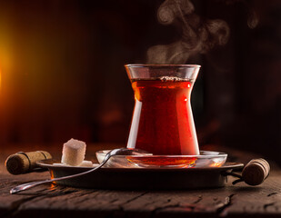 Glass with black traditional turkish tea stands on an old wooden table. Behind a dark background.