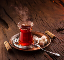 Glass with black traditional turkish tea stands on an old wooden table. Behind a dark background.