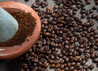 Black coffee ground in a clay mortar and in grains on the surface of a wooden table in sunny rays.
