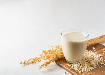 Oat milk in glass with flakes and spike or ears of grain on white background