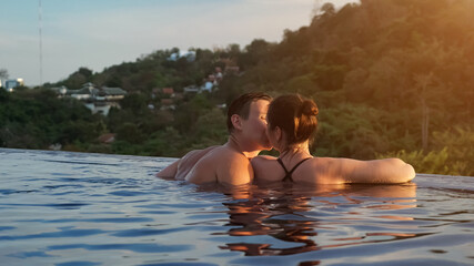 muscular guy approaches brunette leaning and kisses her in outdoor swimming pool