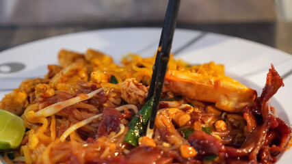 Someone is eating Thai noodles with chopsticks close-up.