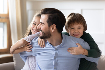 Head shot portrait happy father embracing adorable little children, family having fun together, smiling cute daughter and little son hugging dad from back, looking at camera, posing for photo