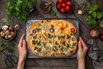 female hands holding  floral painting focaccia,  garden flatbread art, food trend