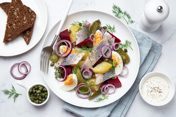herring,  pickled cucumber, beet, potato and eggs salad on white  plate