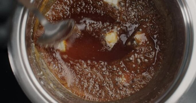 Tabletop slow motion video: confectioner in black gloves adds butter to the boiling melted sugar, chef makes hot caramel, cooking filling for cake, 4k 60fps Prores HQ 10 bit