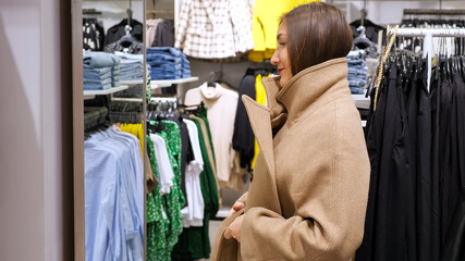 Young woman in a long oversize coat in front of a mirror in a store.