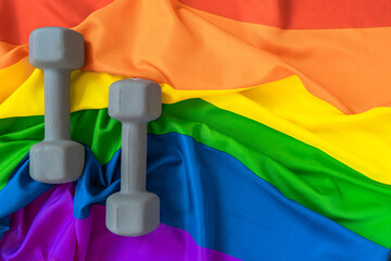 Close-up of dumbbells against the background of the gay pride rainbow symbol of minorities. Copy space. The concept of sports in LGBT.