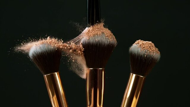 Makeup brushes touch each other on dark background and small particles of cosmetics, super slow motion, 1000 fps.