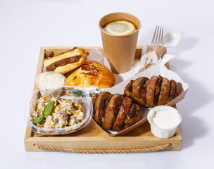 Delicious lunch with disposable tableware on wooden tray. Lemon tea, salad, baked potatoes with meat, sauce and buns.