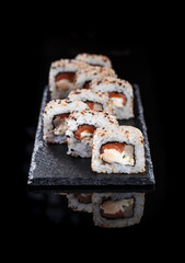 Rolls with salmon, avocado, cucumber on a stone plate on black background.