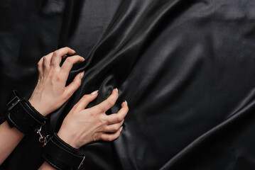 female hands in handcuffs on a dark silk sheet - obrazy, fototapety, plakaty