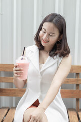 Closeup woman drinking strawberry smoothie and cake with green nature background, selective focus