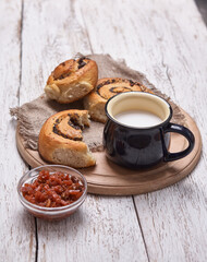 Variety of homemade puff pastry buns cinnamon served with milk cup, jam, butter as breakfast over white plank wooden background. Flat lay, space