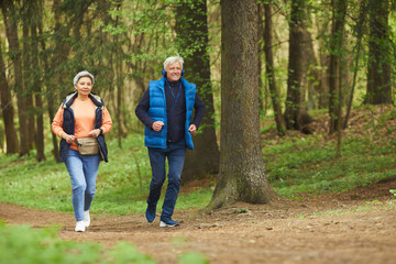 Full length portrait of active senior couple enjoying morning run in beautiful green forest, copy space