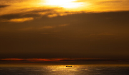 Obraz premium Dramatic golden sunset over ocean with cargo ship in the distance.
