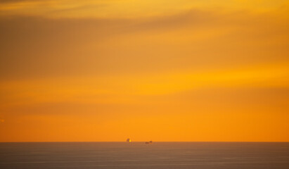 Dramatic golden sunset over ocean with cargo ships in the distance.