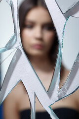 Young woman looks in a broken mirror. Out of focus portrait of beautiful female in the mirror shards