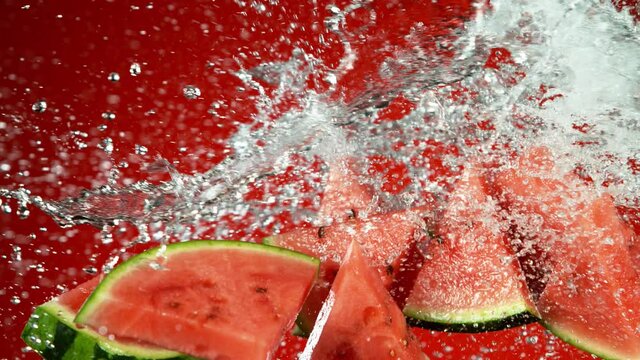 Super slow motion of water melon pieces flying up in the air with water splashes