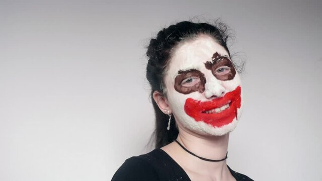 Portrait of girl with joker make up dances then smiles and shows humb up. White background