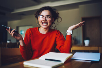 Portrait of cheerful female student laughing sitting in library satisfied with completing coursework making creative solution, smiling hipster girl received message with good advertising offer