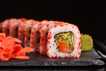 Roll with red caviar of fresh salmon, cream cheese, cucumber, avocado. Served with ginger and wasabi on black ceramic slate.