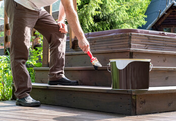 Male painter with a paint brush. A man, Caucasian, paints a wooden terrace.