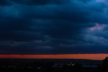 Fototapeta na wymiar Black thunderclouds at sunset. Bright orange sunset and dark clouds. Storm sky