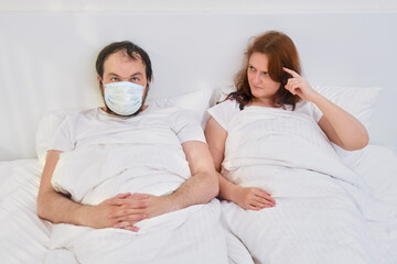 A woman thinks it's crazy to use a medical mask at home. The wife twists her finger at her temple looking at her husband