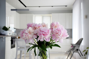 Bouquet of pastel pink peony flowers in bloom with white kitchen on background. Flowers in interior in minimalist style.