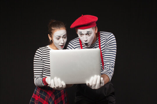 man and woman with white makeup on their faces like mimes looks at a laptop on a black background