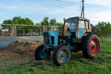 Obraz premium Abandoned old tractor in the village. Blue tractor with red wheel