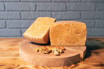 A head of aged cheese cut in half on a wooden Board with various nuts on the background of a brick wall