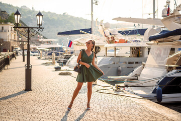 A beautiful woman in a fashionable summer dress and stylish accessories walks in the summer along...