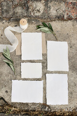 Summer wedding stationery mock-up scene. Blank greeting cards, envelopes, silk ribbon and olive branches on grunge concrete background.Vertical feminine flat lay, top view, no people.