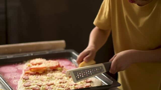 Children cooks pizza. Boy helps father. Prepering ingredients for pizza. Dad rubs cheese on a grater