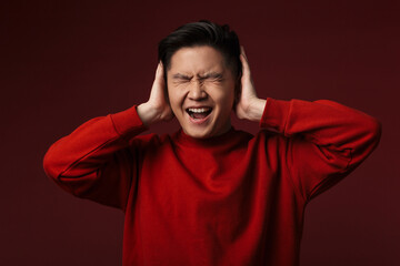 Image of displeased young asian man covering his ears and screaming