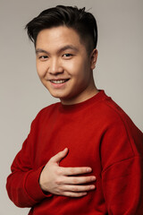 Image of pleased asian man smiling and holding her hand on chest